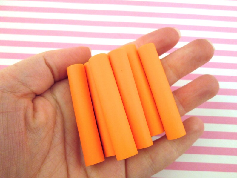 May include: Six orange polymer clay tubes, approximately 1.5 inches long, are held in a hand. The tubes are smooth and have a matte finish.