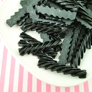 May include: A white plate with a pile of black licorice twists and flat licorice pieces.