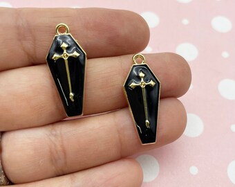 May include: Two black coffin-shaped charms with gold trim and a gold cross design.