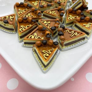 以下が含まれることがあります： 白い皿に、チョコレートチップとキャラメルアイシングで飾られたミニチュアチョコレートケーキのスライスがいくつか並んでいます。ケーキのスライスは、皿の上にランダムに配置されています。