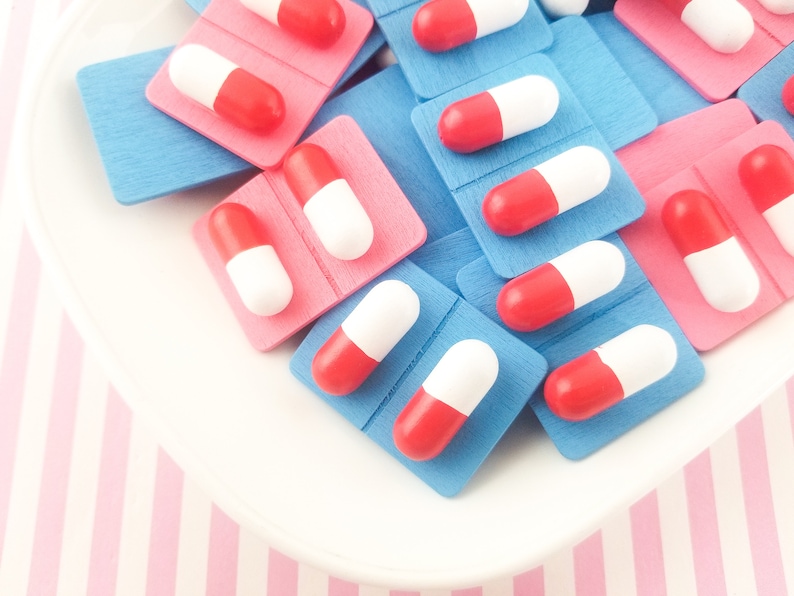 May include: A close-up of a pile of red and white pills in blue and pink pill boxes. The pills are arranged in a random pattern.