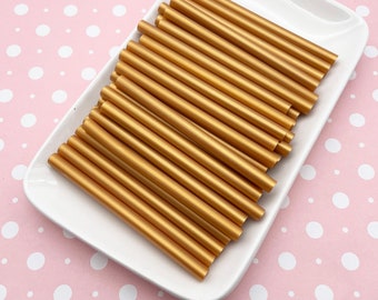 May include: A pile of gold wax sticks on a white plate. The plate is on a pink background with white polka dots.