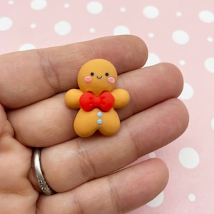 May include: A small gingerbread man figurine with a red bow tie and blue buttons. The figurine is made of polymer clay and is perfect for adding a festive touch to crafts and decorations.