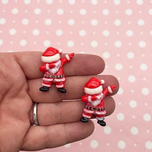 Puede incluir: Dos figuras de Papá Noel rojas y blancas con botas negras y barba blanca. Las figuras de Papá Noel están en una pose de dabbing con el brazo derecho extendido.