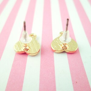 May include: A pair of gold heart-shaped stud earrings with clear plastic backs.