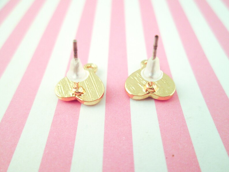 May include: A pair of gold heart-shaped stud earrings with clear plastic backs.