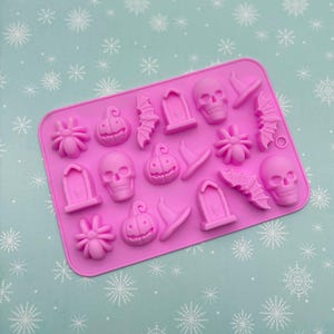May include: A pink silicone mold with Halloween-themed shapes. The mold features a variety of designs, including skulls, pumpkins, bats, spiders, tombstones, and witch hats. The shapes are raised and detailed, perfect for crafting or baking.