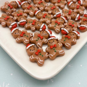 May include: A collection of small, brown gingerbread man figurines with white icing details, red bow ties, and Santa hats. The figurines are arranged on a white, rectangular plate, perfect for holiday crafts or decorations.