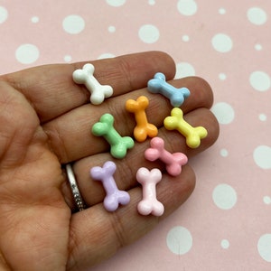 May include: A collection of pastel-coloured plastic bone charms. The charms are in various shades of pink, blue, green, and yellow.