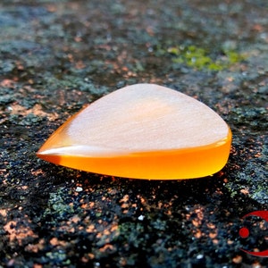 Puede incluir: Primer plano de una púa de guitarra naranja y blanca. La púa está hecha de un material translúcido y tiene una superficie lisa.