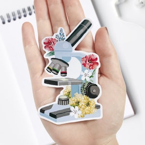 May include: A blue microscope with floral details. The microscope has a black arm and a white base. The flowers are red, white, and yellow.
