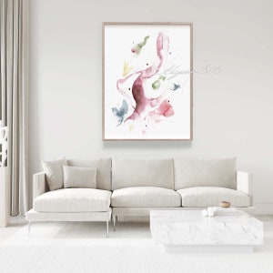 May include: Abstract watercolor painting in shades of pink, green, and yellow. The painting features a large, organic shape with smaller shapes scattered around it. The painting is framed in a light wood frame and is hanging on a white wall.