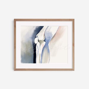 May include: Watercolor painting of a knee joint, framed in a light brown wooden frame. The artwork features anatomical details in shades of white, blue, and pink, with soft brushstrokes. The overall theme is medical art.