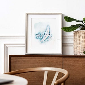 May include: A framed watercolor painting of abstract shapes in shades of blue and white. The painting is set against a white wall with a wooden cabinet and a potted plant in the background.