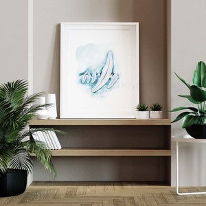 May include: A white framed print with a watercolor painting of a blue and white abstract design. The print is hanging on a shelf with a potted plant and other decor.