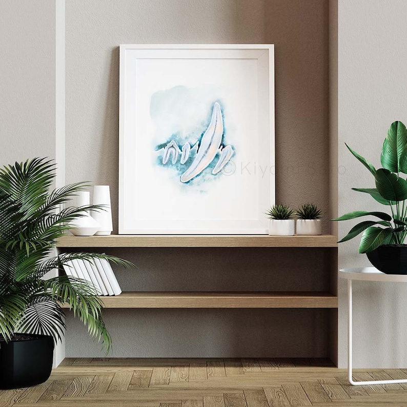 May include: A white framed print with a watercolor painting of a blue and white abstract design. The print is hanging on a shelf with a potted plant and other decor.