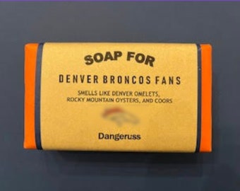May include: A bar of soap with orange and black stripes, featuring the text "SOAP FOR DENVER BRONCOS FANS" and "SMELLS LIKE DENVER OMELETS, ROCKY MOUNTAIN OYSTERS, AND COORS". The text "Dangeruss" is at the bottom of the soap.