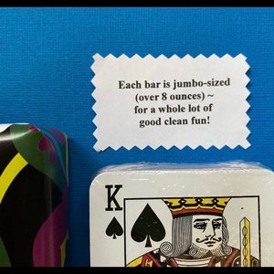 May include: A white card with a black spade and the letter K on it. The card is part of a deck of cards. A white label with the text "Each bar is jumbo-sized (over 8 ounces) ~ for a whole lot of good clean fun!" is visible above the card.