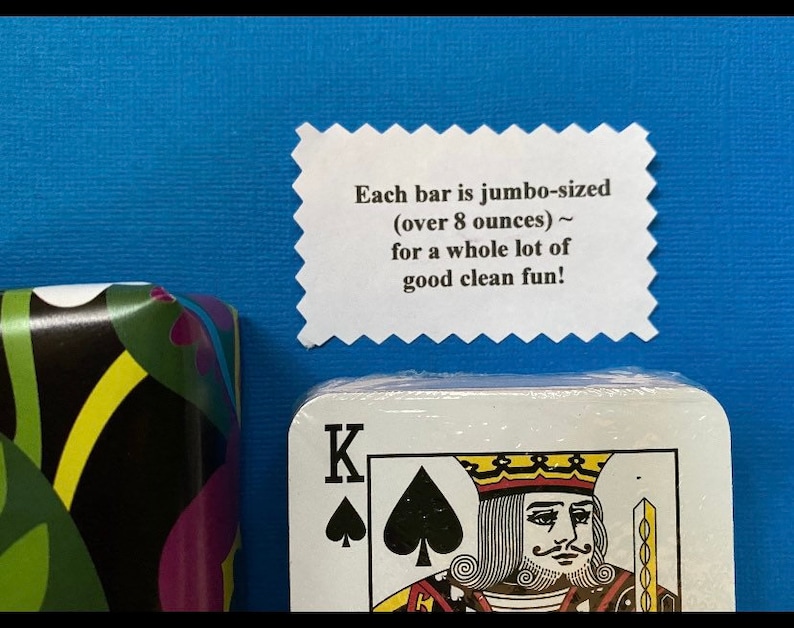 May include: A white card with a black spade and the letter K on it. The card is part of a deck of cards. A white label with the text "Each bar is jumbo-sized (over 8 ounces) ~ for a whole lot of good clean fun!" is visible above the card.