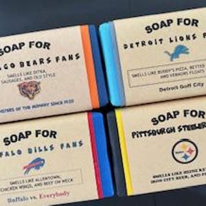 Może przedstawiać: Cztery kostki mydła, każda z logo innego zespołu NFL i opisem zapachu mydła. Mydła są oznaczone jako "SOAP FOR CHICAGO BEARS FANS", "SOAP FOR DETROIT LIONS FANS", "SOAP FOR BUFFALO BILLS FANS" i "SOAP FOR PITTSBURGH STEELERS FANS".