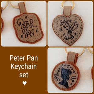 Peut inclure: Ensemble de trois breloques de porte-clés Peter Pan. Les breloques sont en feutre brun et présentent différents personnages et citations de Peter Pan. Les breloques sont attachées à des anneaux de clés dorés.