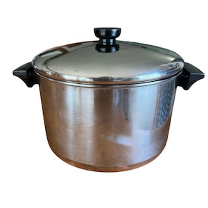 May include: A stainless steel cooking pot with a lid. The pot has a shiny, reflective surface and black handles. The lid has a black knob. The bottom of the pot has a copper-colored band.