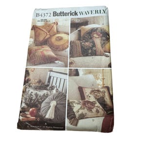 May include: A Butterick B4372 Waverly sewing pattern envelope featuring illustrations of various decorative throw pillows. The designs include square, rectangular, and round cushions with floral, plaid, and solid fabric patterns, some with tassels and fringe accents.