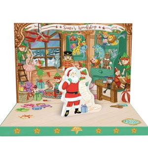 May include: A Christmas pop-up diorama depicting Santa Claus with a list, with the text "Santa's Workshop." The scene includes elves, toys, and a wintery backdrop. The base is green with gold stars.