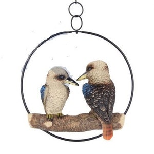 May include: A hanging metal circle with two brown and white birds perched on a branch. The birds have blue accents on their wings and one has an orange tail.
