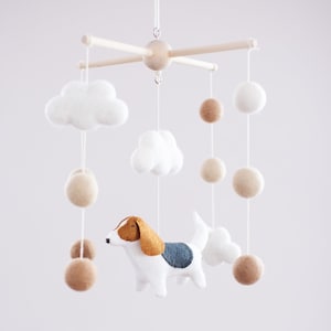 Könnte beinhalten: Ein weißes, braunes und blaues Filz-Babymobil mit einem Hund, Wolken und beigefarbenen Bällen, die an einem Holzrahmen hängen.