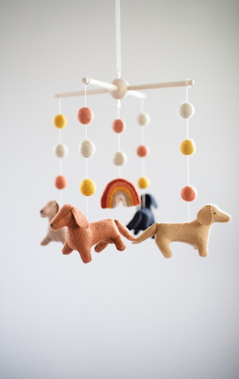May include: A baby mobile with felt dachshund dogs, a rainbow, and colorful pom poms.