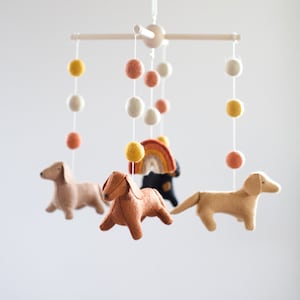 May include: A wooden mobile with felt dachshund dogs, a rainbow, and colorful pom poms hanging from it.