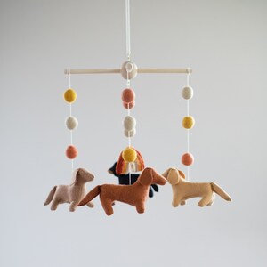 May include: A wooden mobile with felt dachshund dogs, a rainbow, and felt balls in shades of yellow, orange, and white.