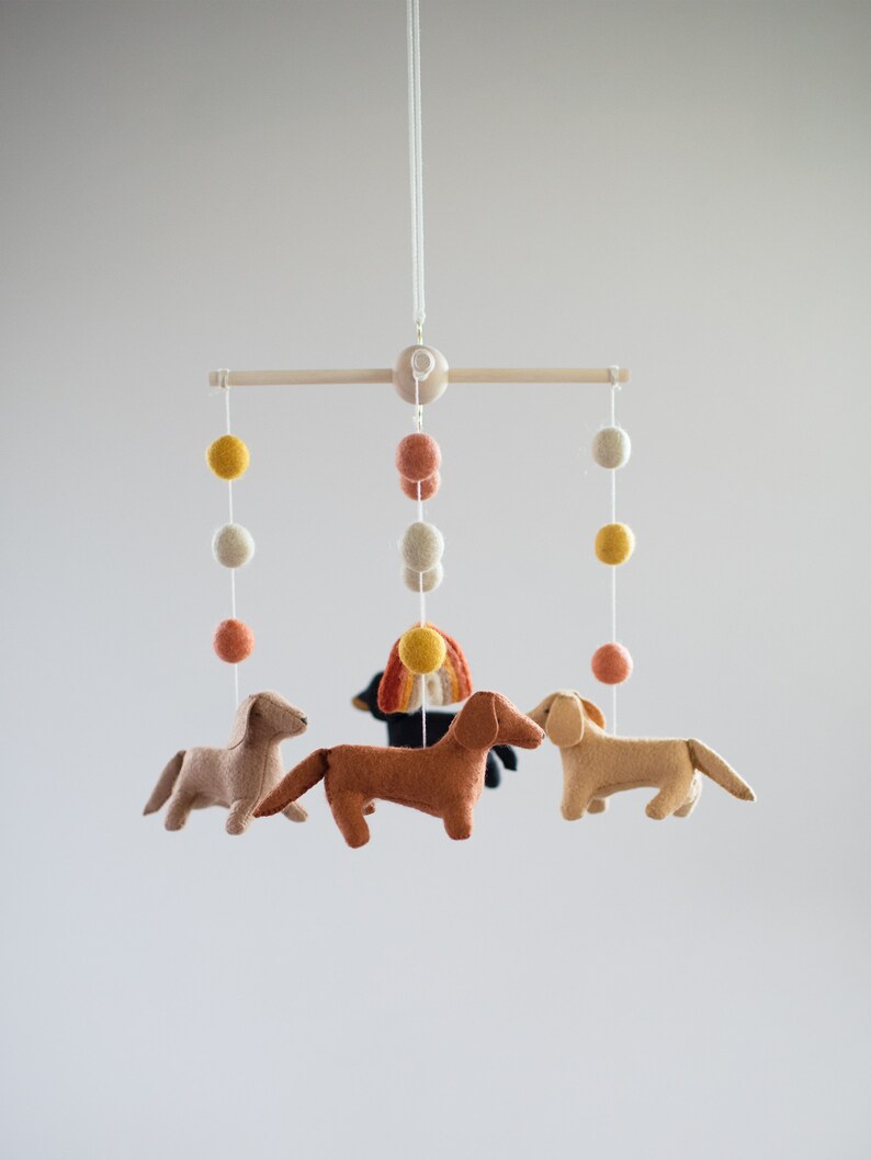 May include: A wooden mobile with felt dachshund dogs, a rainbow, and felt balls in shades of yellow, orange, and white.