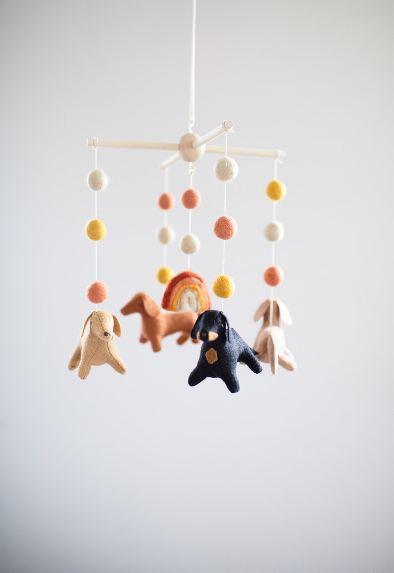 May include: A white wooden baby mobile with felt dachshund dogs, a rainbow, and colorful pom poms.