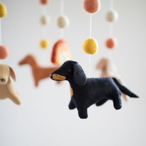 May include: A baby mobile with felt dachshund dogs, a rainbow, and colorful pom poms.