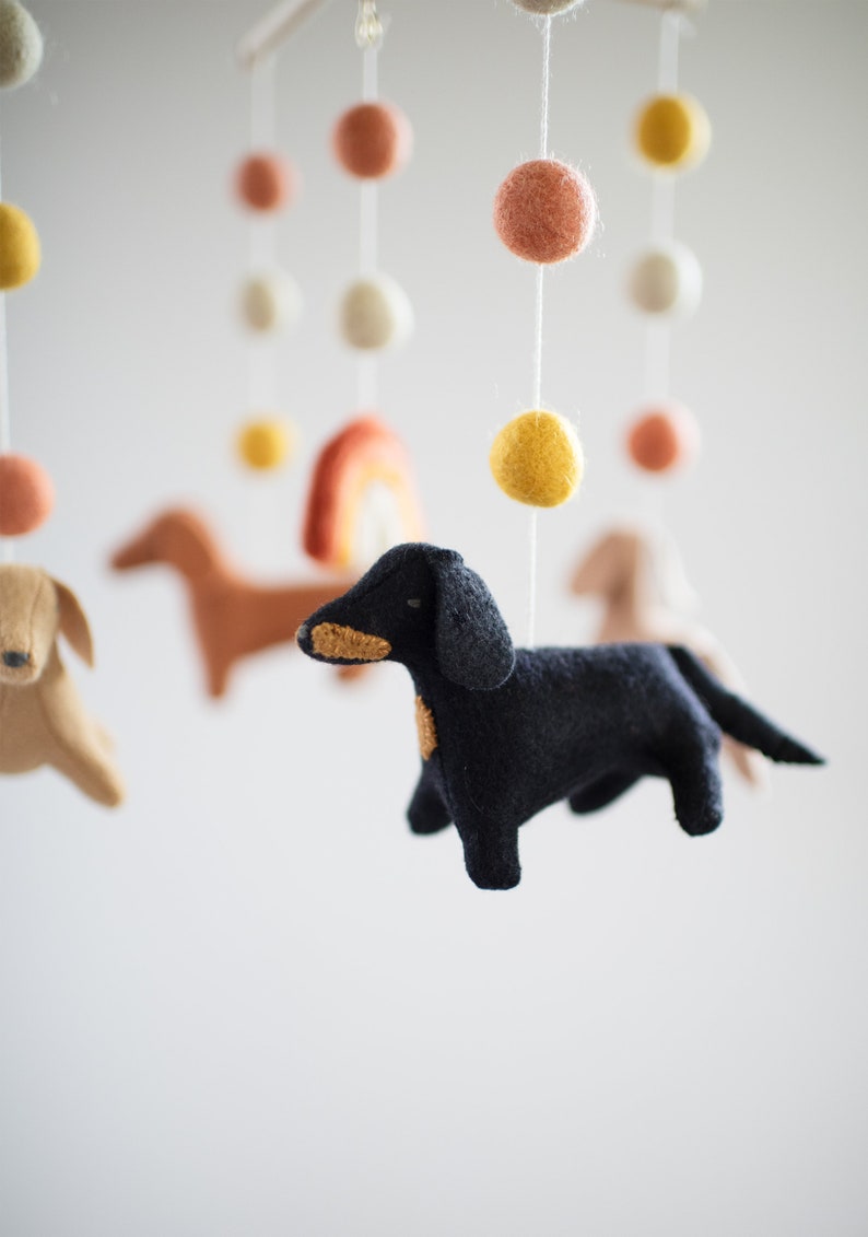 May include: A baby mobile with felt dachshund dogs, a rainbow, and colorful pom poms.
