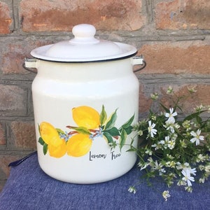 Könnte beinhalten: Ein weißer Emaille-Krug mit Deckel und Henkeln. Der Krug ist mit einem gemalten Design von Zitronen auf einem Zweig mit grünen Blättern und den Worten "Lemon Tree" verziert.