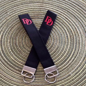 May include: Two black keychains with silver key rings. Each keychain has a red "DD" embroidered on the black fabric.