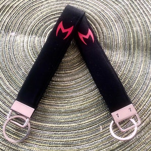 May include: Black key chain with two red M's on the strap. The key chain has two silver key rings.