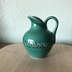 May include: A small green ceramic pitcher with a white inscription that reads "LUXEMBOURG".