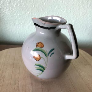 May include: A small, gray ceramic pitcher with a black rim and a floral design in shades of green and orange.