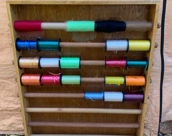 May include: Wooden craft organizer with multiple spools of colorful thread and a roll of brown paper. The thread spools are in various colors, including red, blue, green, orange, and yellow. The organizer is made of light-colored wood.