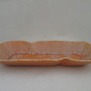 May include: A long, rectangular ceramic serving dish with a light orange glaze and white marbling. The dish has a slightly wavy edge.