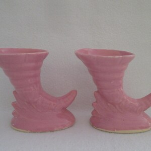 May include: Two pink ceramic vases shaped like a boot with a pointed toe. The vases are in the shape of a boot with a pointed toe. The vases are in the shape of a boot with a pointed toe.