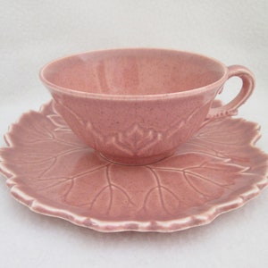 May include: A pink teacup and saucer set with a leaf design. The cup and saucer are both made of ceramic and have a glossy finish.