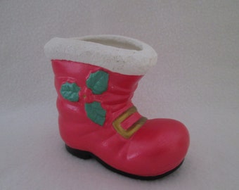 May include: A red ceramic Santa boot planter with a white fur trim, green holly leaves, and a gold buckle.