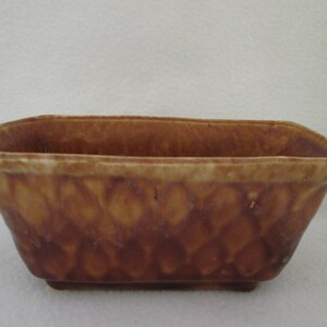 May include: A rectangular brown ceramic planter with a mottled glaze. The planter has a slightly squared shape and a smooth, glazed finish.
