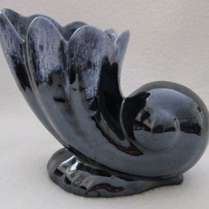 May include: A black ceramic vase with a glossy finish and a unique, abstract shape. The vase has a wide opening and a narrow base, and it is designed to hold flowers or other decorative items.