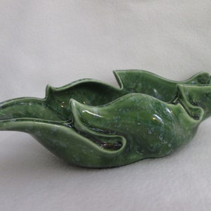 May include: A green ceramic bowl with a unique, organic shape. The bowl is glazed with a speckled green finish.